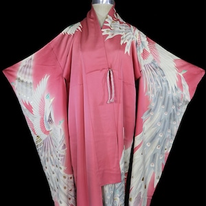 May include: A pink silk kimono with a white and grey peacock design. The kimono has a long, flowing silhouette and is perfect for special occasions.