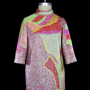 Puede incluir: Un vestido de lentejuelas rosa, verde, amarillo y rojo con un patrón abstracto. El vestido tiene cuello alto y mangas tres cuartos.