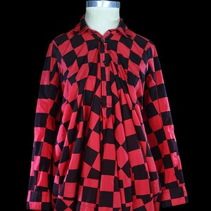 May include: A red and black checkered long-sleeved shirt with a gathered, loose fit. The shirt has a button-up front and a collar.