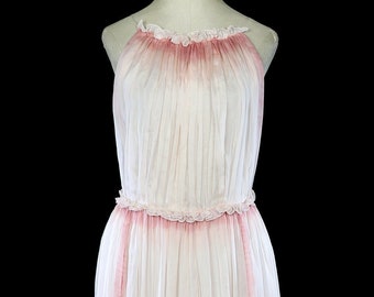Puede incluir: Un vestido largo y fluido de color blanco con un efecto degradado rosa. El vestido tiene un escote halter y un ribete con volantes en la parte superior y la cintura. El vestido está hecho de una tela transparente y tiene una falda fluida.