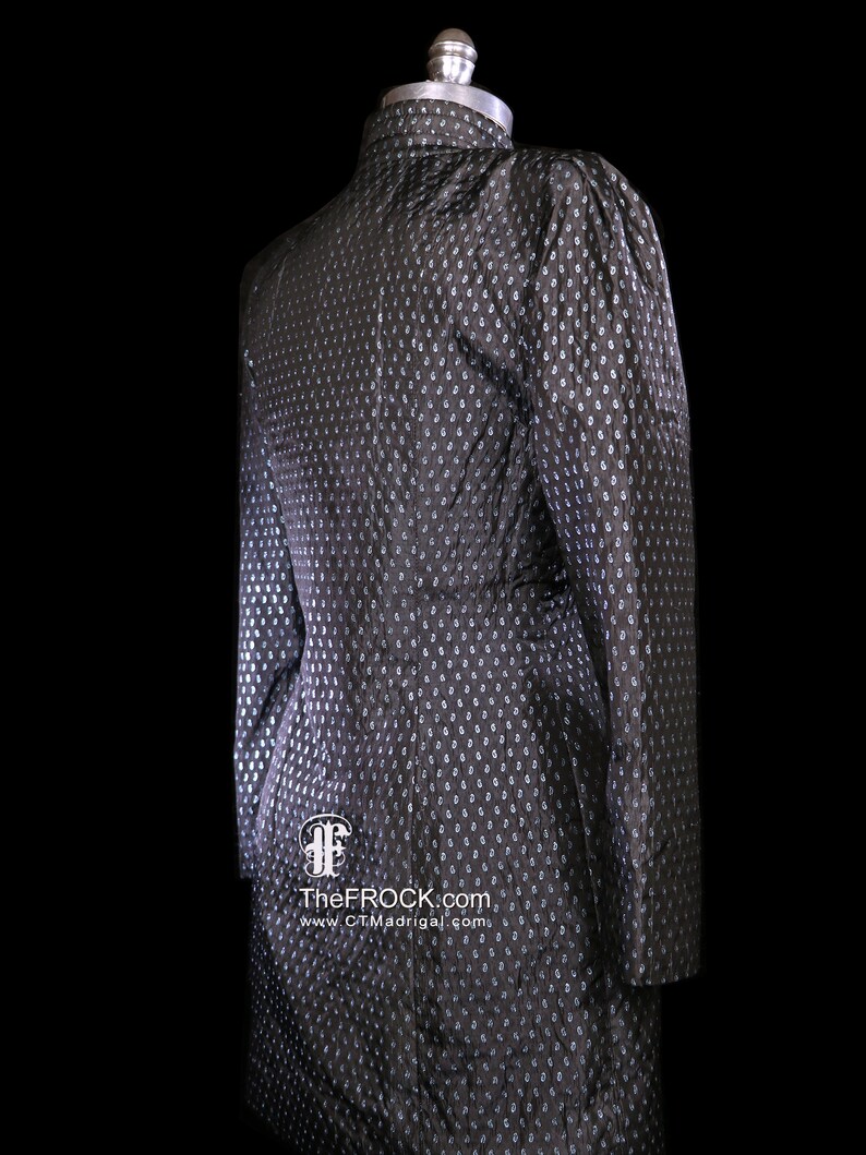 May include: A black and silver patterned dress with a high collar and long sleeves. The dress is on a mannequin and has a small logo on the bottom.