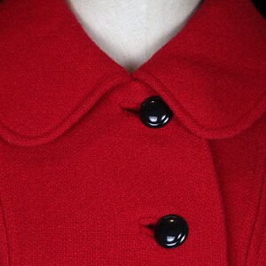 May include: A red wool coat with a Peter Pan collar and two black buttons. The coat is made of a textured fabric.