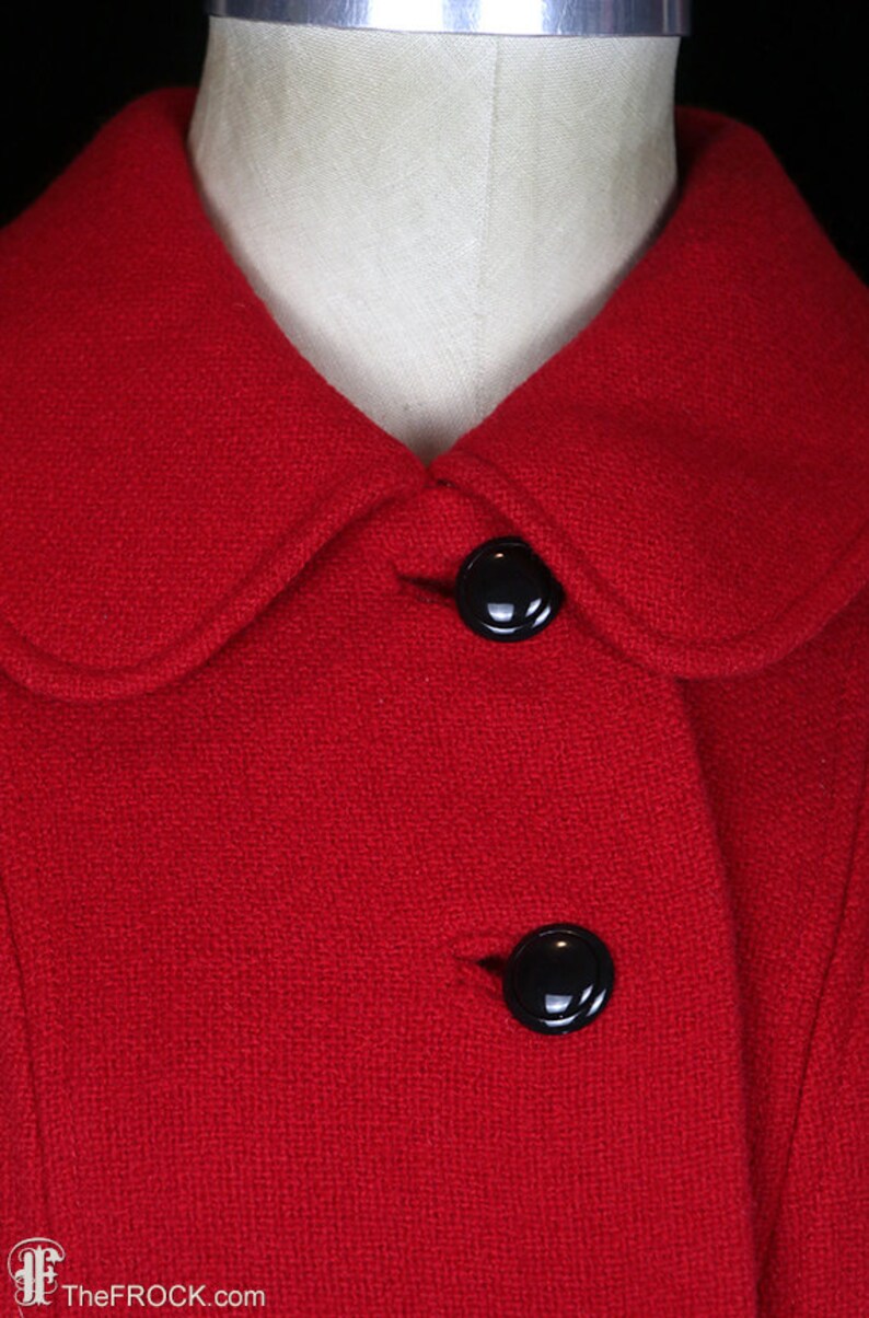 May include: A red wool coat with a Peter Pan collar and two black buttons. The coat is made of a textured fabric.