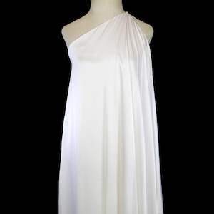 Peut inclure: Une robe blanche à une épaule drapée sur un mannequin. Le tissu est lisse et fluide, avec des plis souples. La robe est de couleur blanche unie et semble être faite d'une matière légère. TheFROCK.com et Instagram @thefrockdotcom sont visibles.