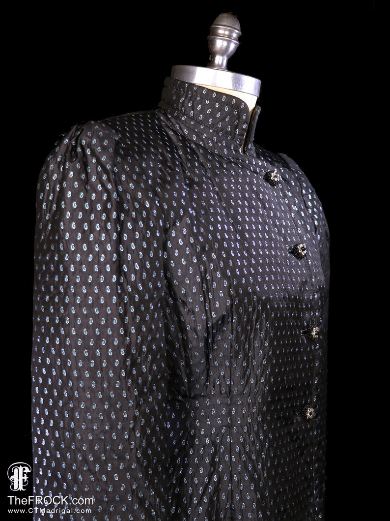 May include: A black and blue patterned dress with a high collar and button closures. The dress is on a mannequin.