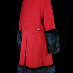May include: A long red coat with black fur trim on the cuffs and hem. The coat has a single button closure at the waist.