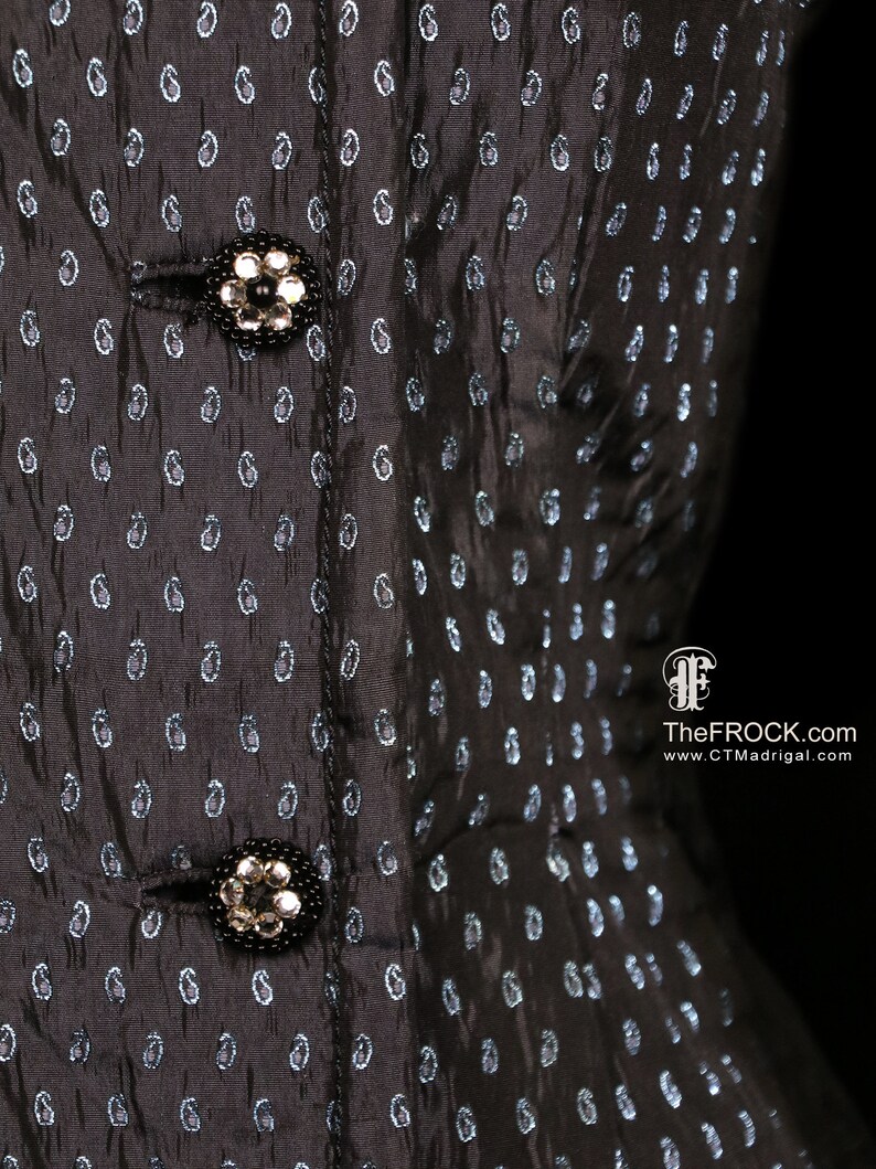 May include: Black dress with a paisley pattern and two silver buttons. The dress has a fitted bodice and a full skirt.