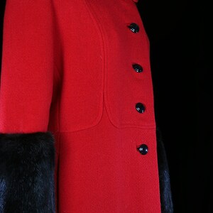 May include: A red wool coat with black fur trim on the cuffs. The coat has a Peter Pan collar and six black buttons down the front.