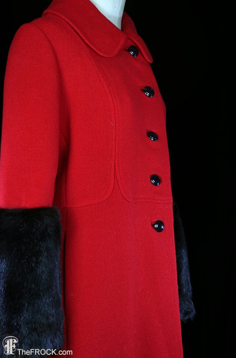 May include: A red wool coat with black fur trim on the cuffs. The coat has a Peter Pan collar and six black buttons down the front.