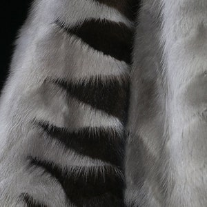 May include: Close-up of a gray and black striped fur fabric. The fur is soft and fluffy, with a subtle sheen.