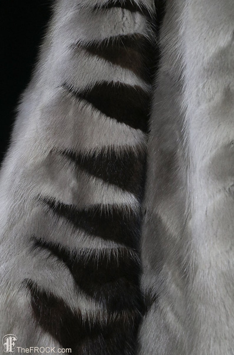 May include: Close-up of a gray and black striped fur fabric. The fur is soft and fluffy, with a subtle sheen.