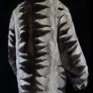 May include: A brown and white fur coat with a geometric pattern. The coat is on a mannequin and has long sleeves.