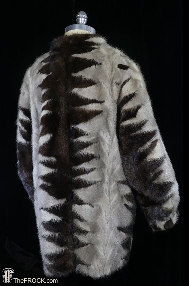 May include: A brown and white fur coat with a geometric pattern. The coat is on a mannequin and has long sleeves.