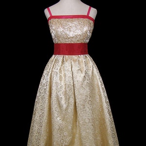 May include: A gold brocade dress with a red satin sash. The dress has a fitted bodice and a full skirt.