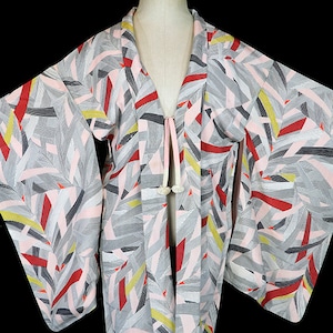 May include: A vintage Japanese kimono with a geometric pattern in shades of pink, gray, red, and yellow. The kimono has a long, flowing silhouette and a tie closure at the front.