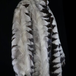 May include: A white and brown fur coat with a striped pattern. The coat is on a mannequin and is shown from the side.