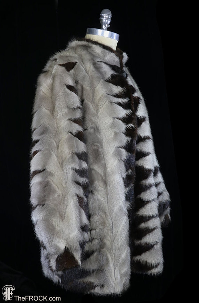 May include: A white and brown fur coat with a striped pattern. The coat is on a mannequin and is shown from the side.