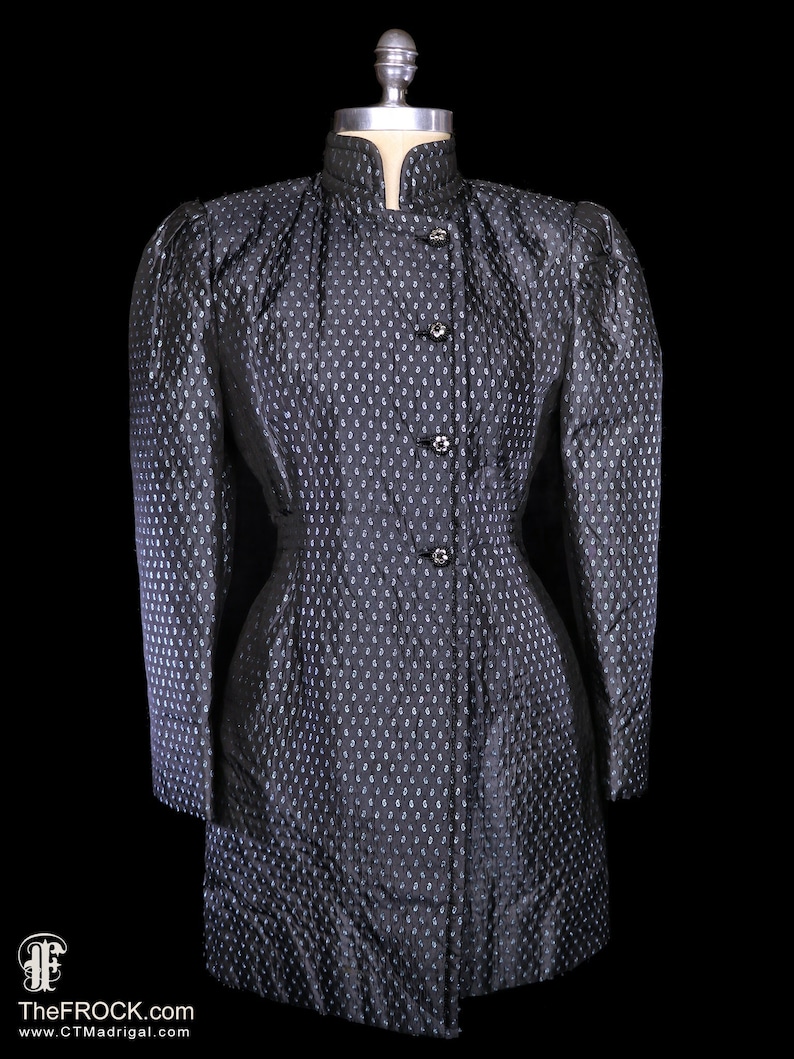 May include: A black quilted jacket with a stand-up collar and button closure. The jacket has a fitted silhouette and a subtle pattern of small white dots.