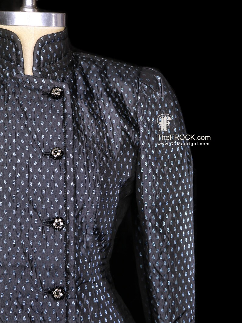 May include: A black and blue patterned jacket with a mandarin collar and decorative buttons. TheFROCK.com and www.CTMadrigal.com are printed on the jacket.