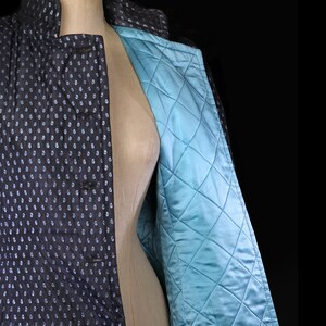 May include: A black quilted jacket with a white polka dot pattern and a teal blue quilted lining. The jacket has a mandarin collar and a button closure.
