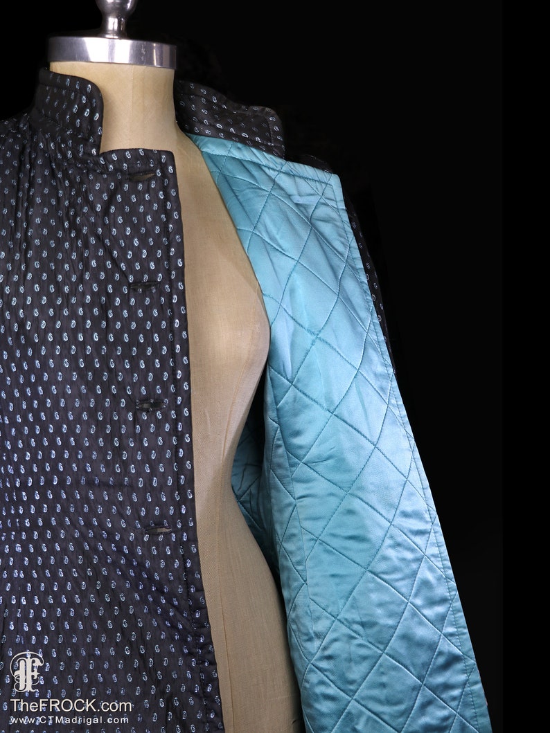 May include: A black quilted jacket with a white polka dot pattern and a teal blue quilted lining. The jacket has a mandarin collar and a button closure.