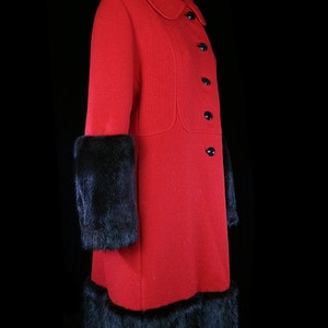 May include: A red wool coat with black fur trim on the cuffs and hem. The coat has a collar and buttons down the front.