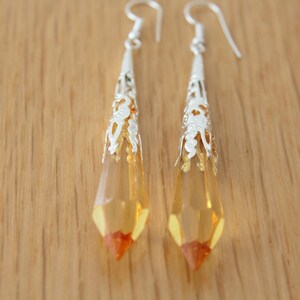 May include: A pair of silver dangle earrings with amber-colored teardrop-shaped crystals.