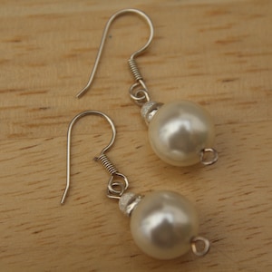 Puede incluir: Un par de pendientes de plata con cuentas blancas de imitación de perlas. Los pendientes tienen un diseño sencillo con cierre de gancho.