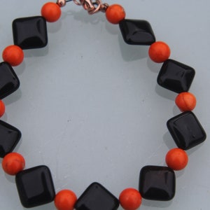 Könnte beinhalten: Ein schwarz-orangenes Armband mit schwarzen rautenförmigen Perlen und orangen runden Perlen.