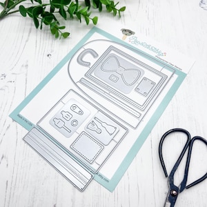 May include: A metal die-cutting template for a backpack with a bow, a zipper, and other details. The template is on a light blue background with the text "Photopolymer Clear Stamps" and "Made in the USA".