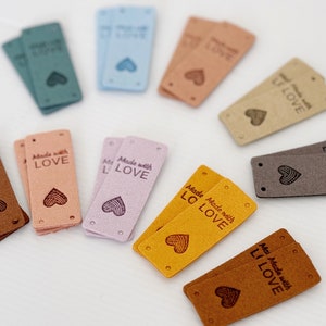 May include: Assortment of colorful leather labels with the text "Made with Love" and a heart design. The labels are in various colors, including brown, pink, blue, and yellow.