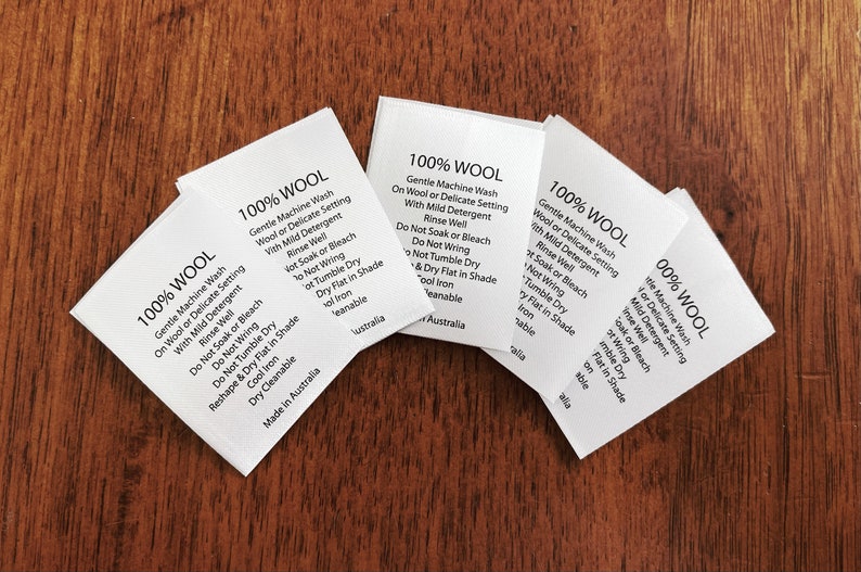 May include: Close-up of five white fabric care labels with black text. Each label reads "100% WOOL" and includes instructions for gentle machine washing, hand washing, and drying. The labels are made in Australia.