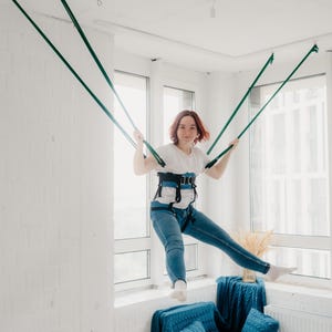 Pode incluir: Um sistema de arn&ecirc;s de suspens&atilde;o azul e preto com al&ccedil;as ajust&aacute;veis e suporte de cintura acolchoado, conectado a quatro cordas verde-escuras ancoradas ao teto, projetado para fitness a&eacute;reo ou atividades de movimento terap&ecirc;utico.