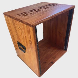 May include: A wooden studio rack enclosure with a natural brown wood grain finish. The top panel features three wavy ventilation cutouts. The front edges include black metal rack rails with numbered mounting holes and a black handle on the side.