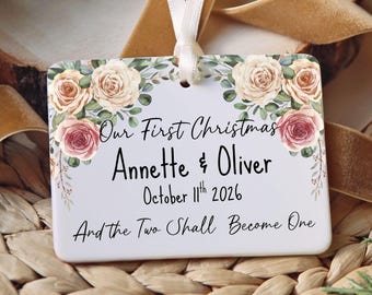 May include: A rectangular white ornament with a white ribbon hanger, featuring a floral design of pink and cream roses. The text reads: Our First Christmas, Annette & Oliver, October 11th 2026, And the Two Shall Become One.