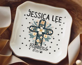 May include: A square white ceramic trinket dish with rounded corners, featuring a black polka dot pattern, a central floral cross illustration, and the text JESSICA LEE, Baptized, and the date 8/23/26 printed in black ink.