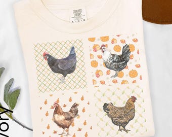 May include: An ivory t-shirt featuring a grid of four square illustrations. Two squares show chickens against a green lattice background, while the other two show chickens surrounded by orange pumpkins and autumn leaves. The neck label reads Comfort Colors.