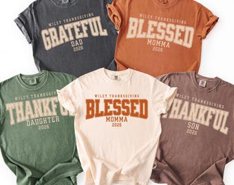 May include: Five short-sleeved crew neck t-shirts in charcoal, orange, green, cream, and brown. Each shirt features the text 'WILEY THANKSGIVING' above a large word like 'GRATEFUL', 'BLESSED', or 'THANKFUL', followed by a family role and '2026'.