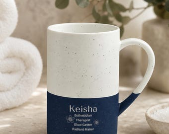May include: A two-toned ceramic mug with a speckled white upper half and a solid navy blue lower half. The navy section features the white text Keisha, Esthetician, Therapist, Glow Getter, Radiant Maker, and two small flower icons.