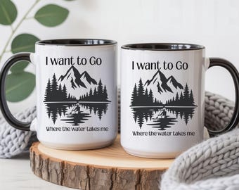 May include: Two white ceramic mugs with black handles and rims. Each mug features a black graphic of mountains, pine trees, and a person in a canoe on water. The text "I want to Go" and "Where the water takes me" is printed in black.