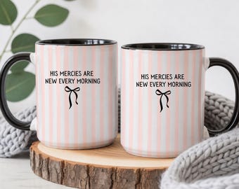May include: Two ceramic mugs featuring a light pink and white vertical striped pattern. Each mug has a black handle and rim, with the black text "HIS MERCIES ARE NEW EVERY MORNING" printed above a small black bow graphic on the front.