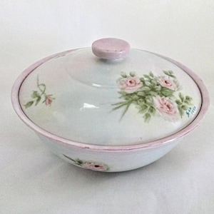 May include: A white ceramic bowl with a pink rim and lid. The bowl and lid are decorated with hand-painted pink roses and green leaves.