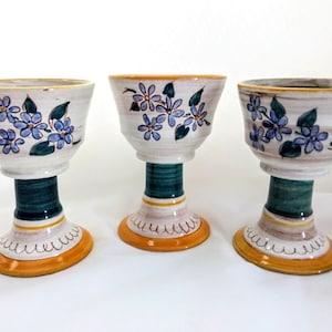 May include: Three ceramic cups with a white base, blue and green floral designs, and a yellow and green base.