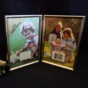 May include: A gold-toned double picture frame with a beaded border. The frame is designed for 35mm prints and has a non-glare glass. The size of the frame is 3 1/2 x 5 inches.