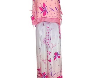 May include: A two-piece outfit featuring a pink floral print. The top is a sleeveless design with a V-neck and tie details. The matching pants are wide-legged with a similar floral pattern, creating a coordinated ensemble. The outfit is displayed on a mannequin.