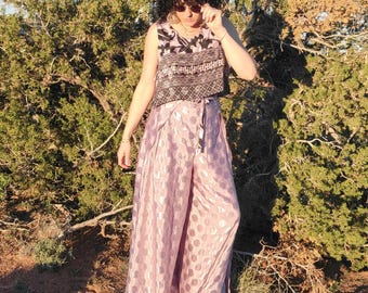 May include: A sleeveless top with a black and white patterned design paired with wide-leg, light pink pants. The pants have a subtle polka dot pattern and a matching tie. The outfit is worn outdoors with a backdrop of green foliage and a clear blue sky.
