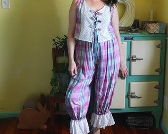 Peut inclure: Un ensemble deux pièces composé d'un haut sans manches et d'un pantalon assorti à motif écossais rose, bleu et blanc. Le haut présente un panneau avant en dentelle anglaise blanche avec trois rubans, et le pantalon a des volants en dentelle.