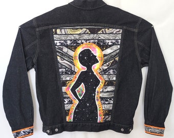 May include: A black denim jacket with a colorful, abstract design on the back. The design features a silhouette of a person with a galaxy background and a bright orange halo.