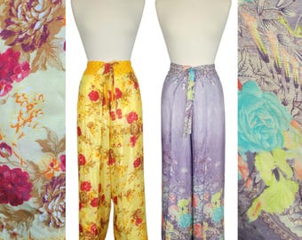 May include: Two pairs of floral print palazzo pants. One pair is yellow with red flowers, the other is purple with blue and green flowers. Both have a drawstring waist. The fabric has a silky sheen.