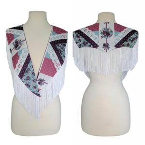 May include: A shawl featuring a patchwork design with floral and geometric patterns in shades of burgundy, light blue, and white. The garment has a deep V-neckline and is finished with long white fringe trim along the edges, displayed on a mannequin.
